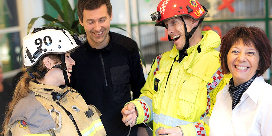 två brandmän, en tjej och en kille, ler och skrattar mot varandra, två ytterligar personer skrattar mot kameran