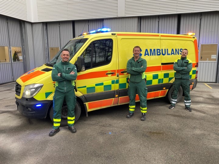 tre personer i grön uniform framför en gul ambulans 