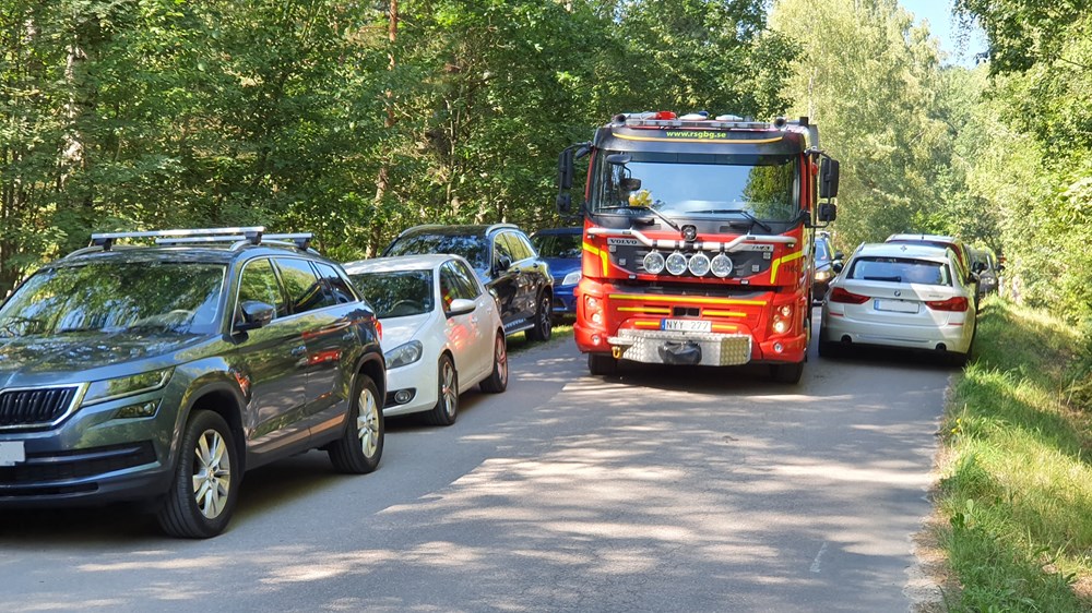 En brandbil som försöker komma fram på en grusväg där bilar parkerat på båda sidor