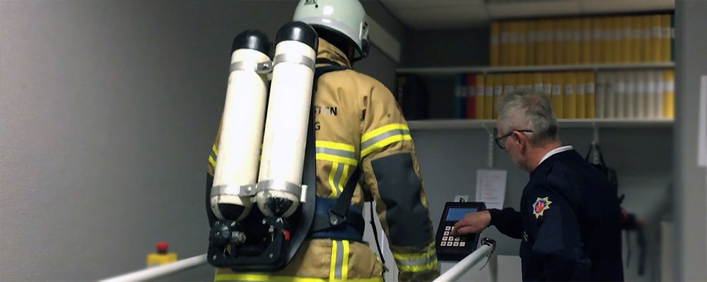 En brandman som går på ett rullband och får stöd av en testledare